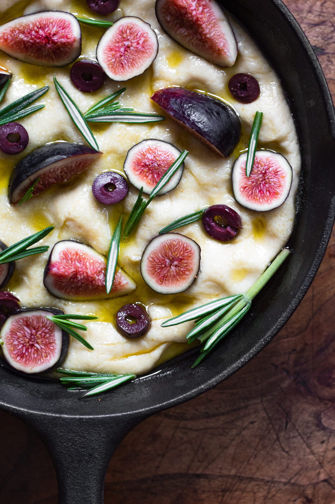 focaccia dough topped with figs, rosemary, and olives in skillet