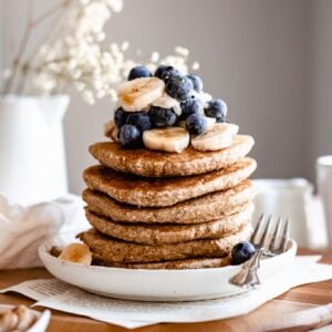 stack of fluffy banana oatmeal pancakes on wooden board with blueberries and bananas