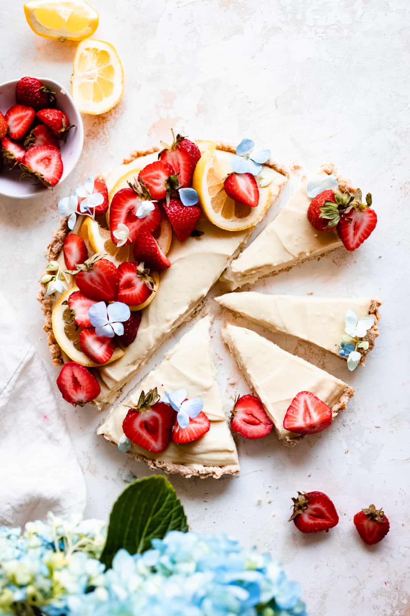 sliced lemon tart with strawberries and hydrangea next to it