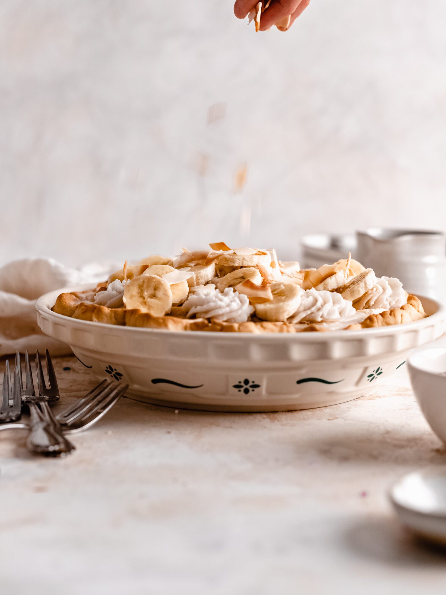 hand sprinkling coconut flakes onto banana cream pie