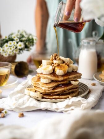 stack of vegan banana pancakes with hand pouring maple syrup over them