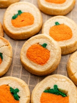 Round slice-and-bake cookies with an orange pumpkin shape and green stem embedded in the center, arranged on parchment paper.