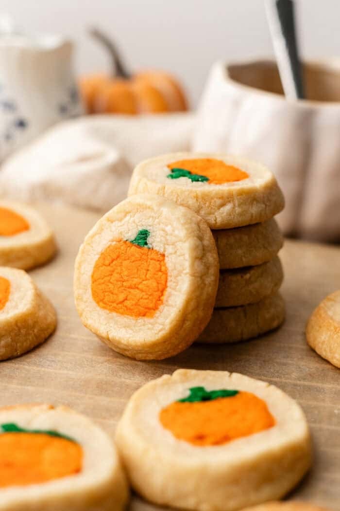 A stack of round shortbread cookies with a decorative orange pumpkin design in the center, surrounded by more cookies on parchment paper.