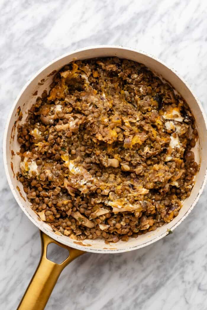 A saucepan with cooked lentils and vegetables mixed together on a white marble surface.