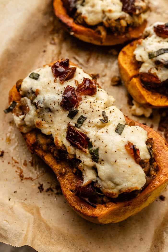 A roasted butternut squash half stuffed with a lentil mixture, topped with melted cheese, herbs, and bits of sun-dried tomato, resting on parchment paper.