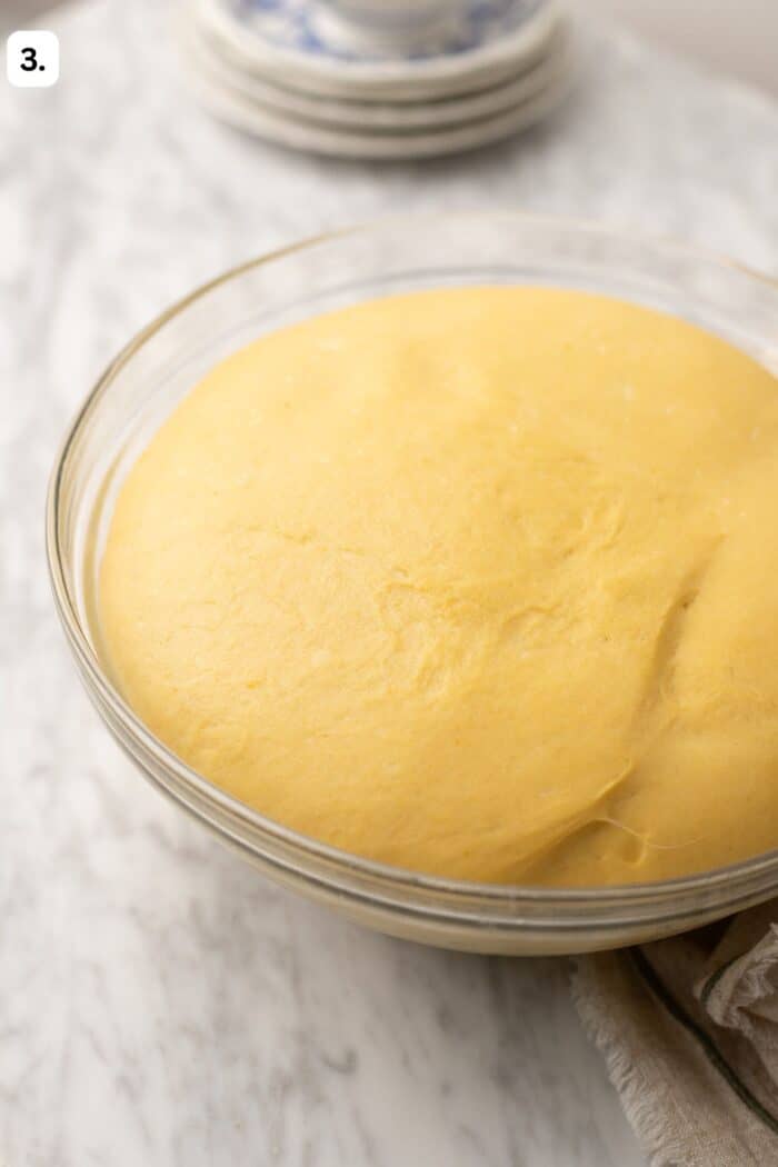 proofed doughnut dough in a bowl on a marble countertop.