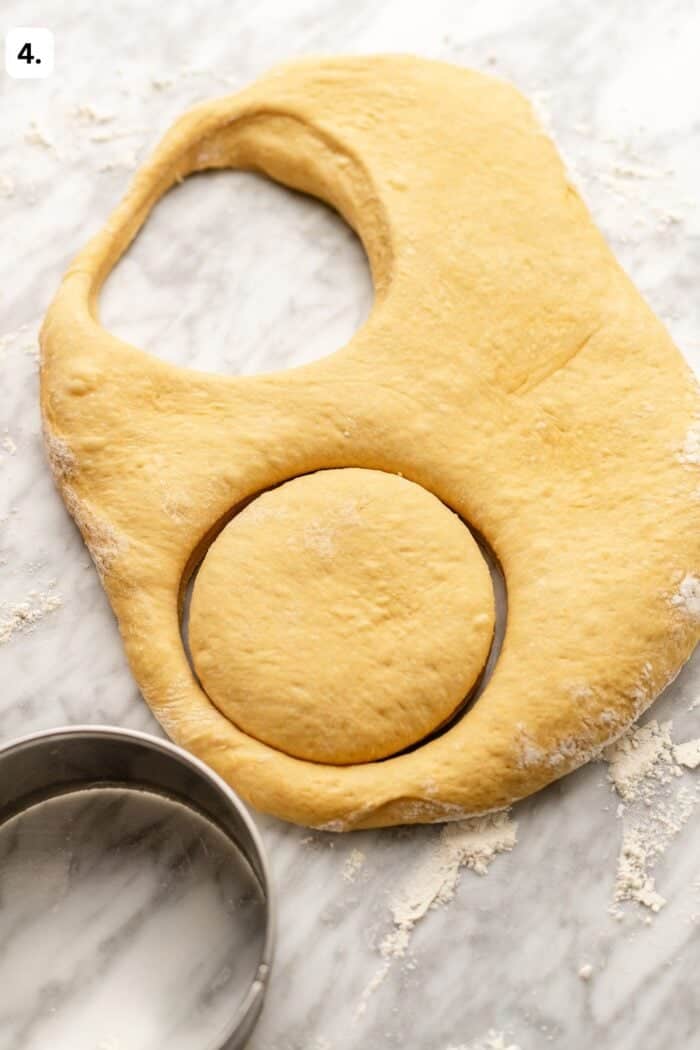 doughnut cutter cutting doughnuts out of the dough on a marble countertop.