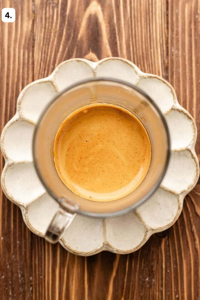 Top-down view of a glass cup of espresso with crema on a scalloped saucer.