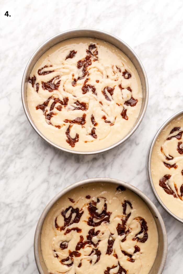 Two round cake pans filled with raw cake batter swirled with fruit jam.