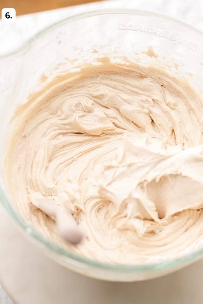 A glass mixing bowl filled with creamy, light tan frosting.