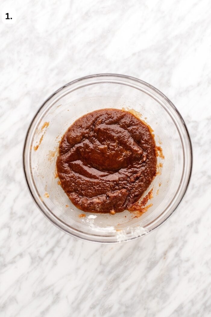 A glass bowl containing a smooth, dark brown mixture on a white marble surface.