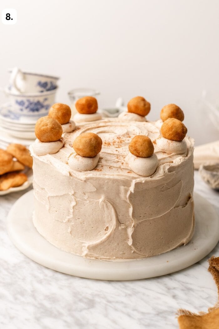 A frosted layer cake topped with swirls of frosting and small fried dough balls.