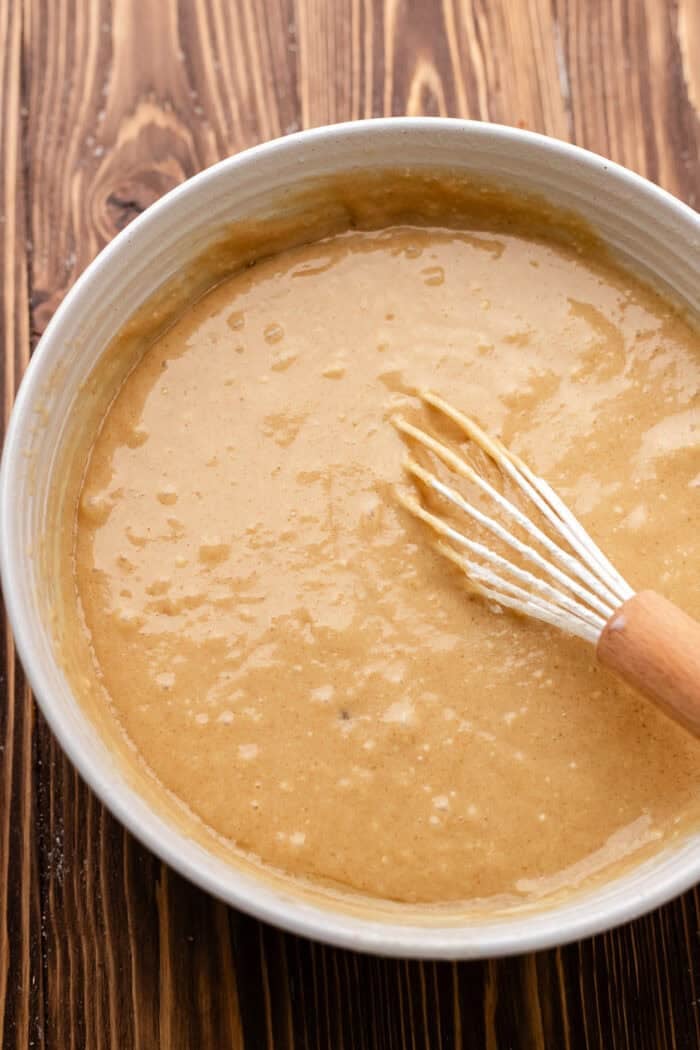 cake batter mixed in a bowl with a whisk on a wooden table.