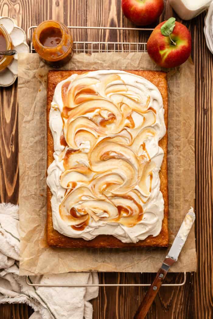 frosted apple spice cake with caramel on top on a cooling rack.