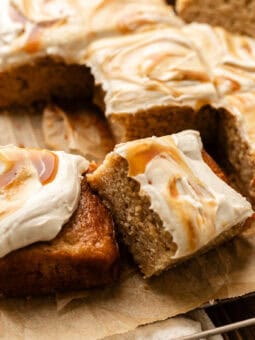 sliced apple spice cake leaning on another slice on a cooling rack with parchment paper on a wooden table.