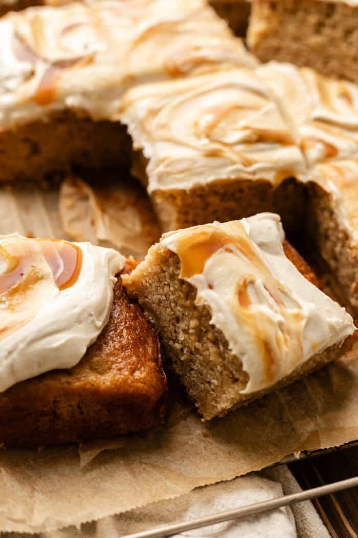 sliced apple spice cake leaning on another slice on a cooling rack with parchment paper on a wooden table.