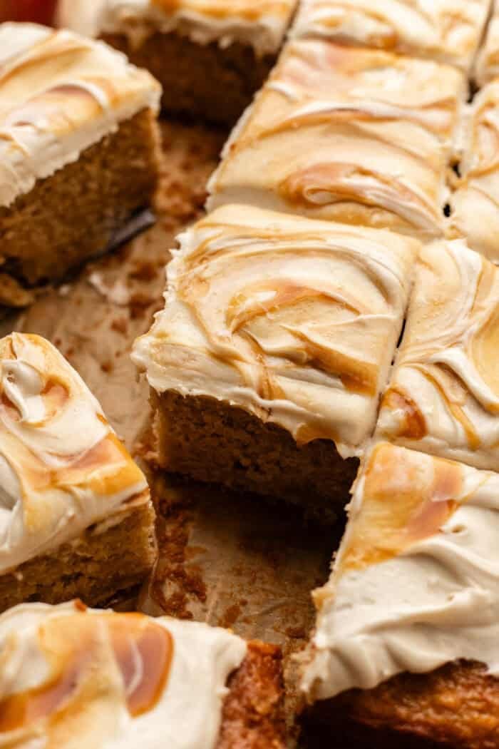 sliced apple spice cake with caramel on the cream cheese frosting on parchment paper.
