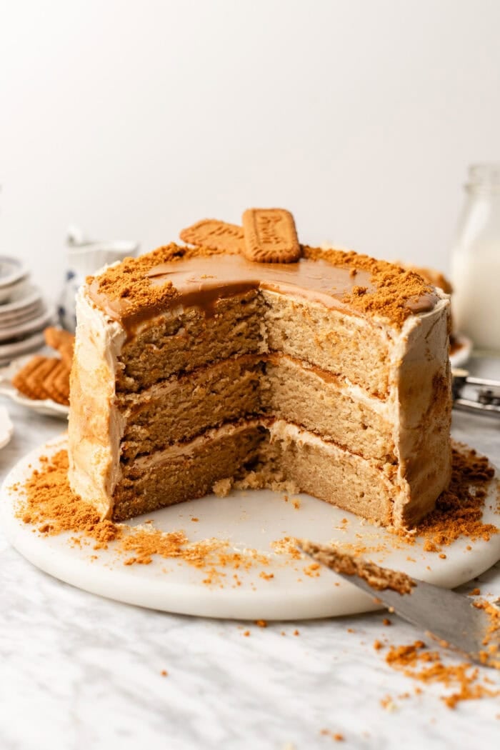 Four-layer cake with brown and white icing, topped with two rectangular cookies and cookie crumbs, sits on a marble surface with a large slice missing. A knife and more crumbs are nearby.
