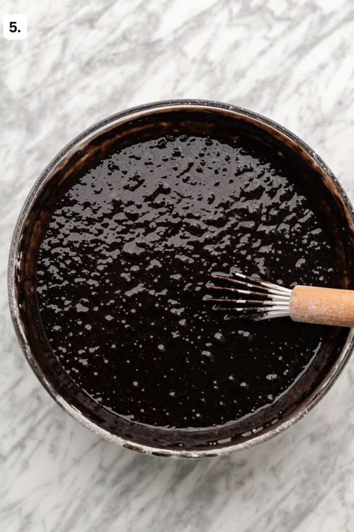Bowl with a whisk whisking the chocolate cake batter on a marble table.