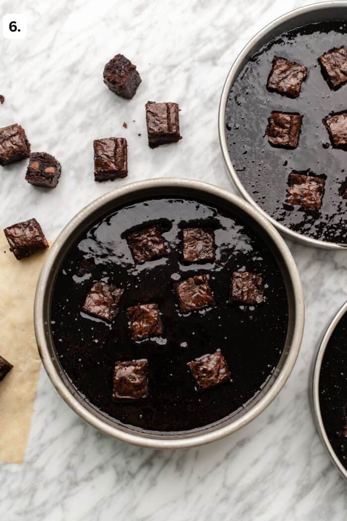 brownie cake batter sprinkled with brownie bites in the cake pans on a marble table before baking.