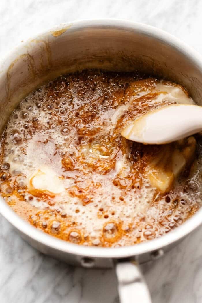 stirring in vegan butter into the melted caramel sugar on a marble table in a saucepan.