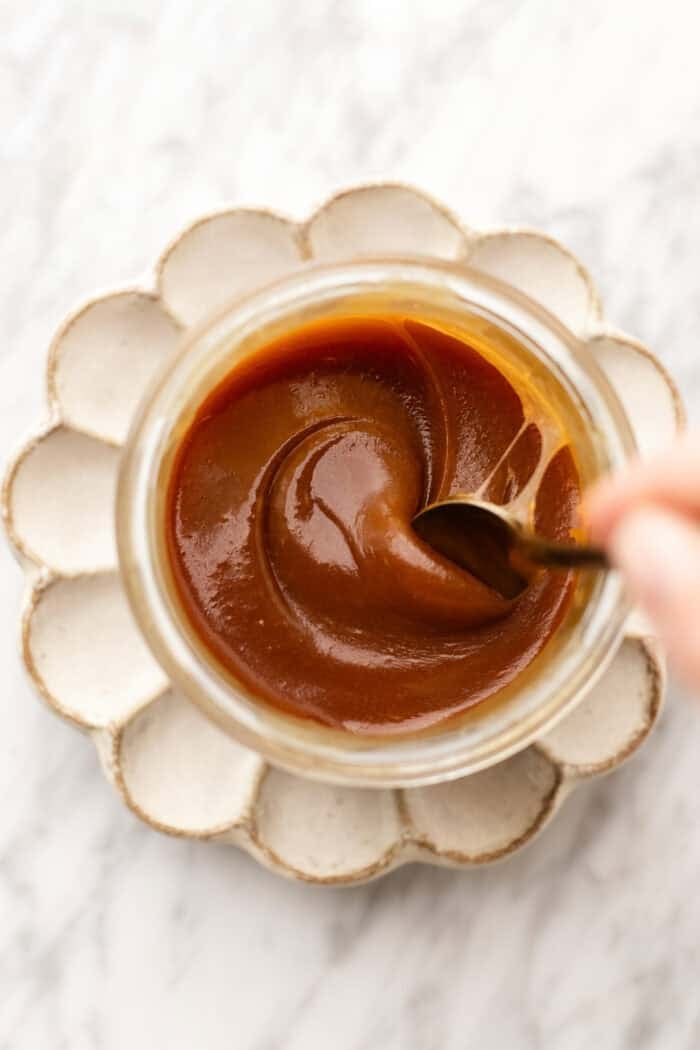 stirring the vegan caramel in a jar on a petal plate on a marble table.