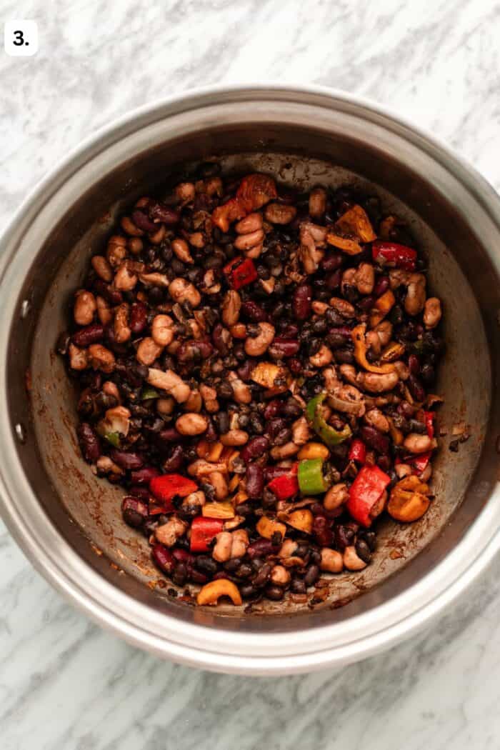 Large pot sautéing the onions, garlic, beans, peppers, and spices together on a marble table.