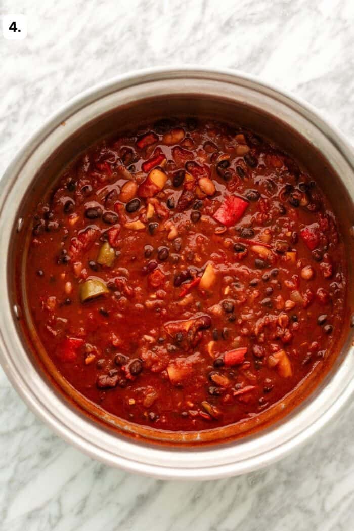 Large pot with three bean chili in it thickening displayed on a marble table.