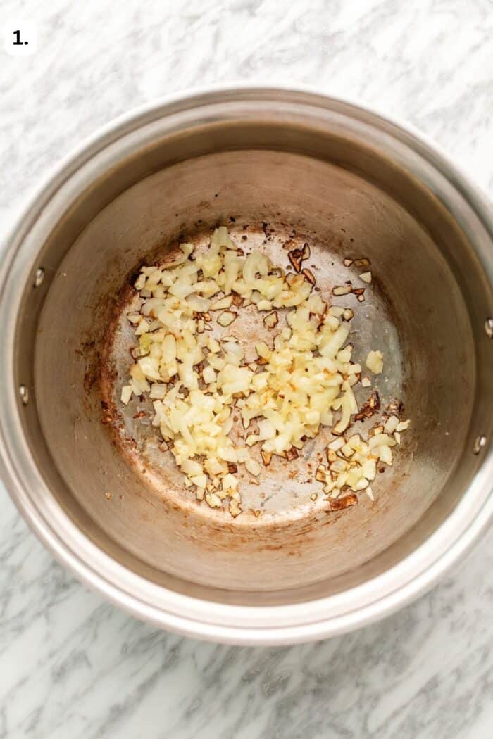 Large pot sautéing the onions and garlic together on a marble table.
