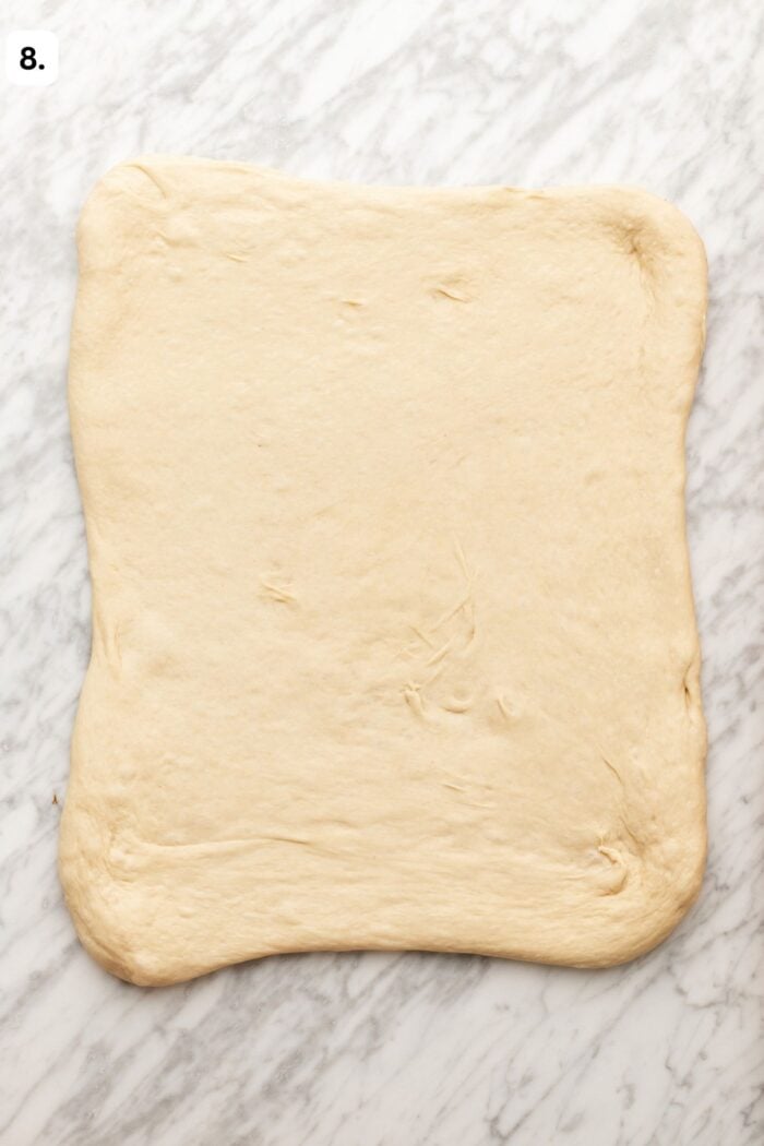Rectangle of raw dough rolled out on a marble surface, ready for further preparation. Small number 8. in the top left corner.