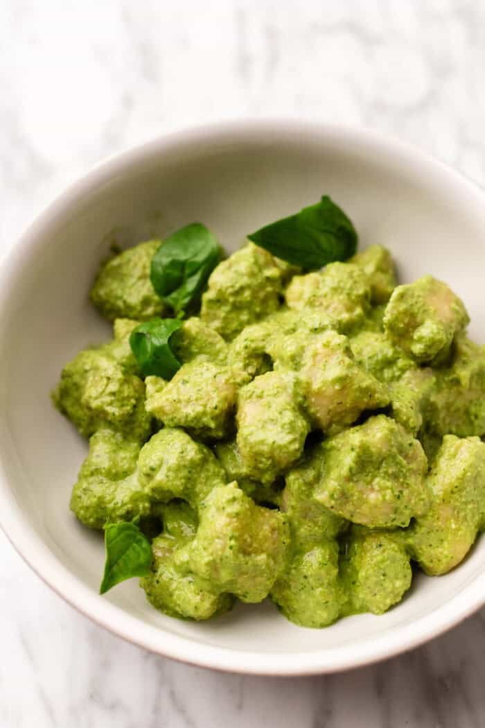 bowl of creamy pesto gnocchi with fresh basil on top.