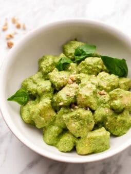bowl of creamy pesto gnocchi with fresh basil and crushed walnuts on top.