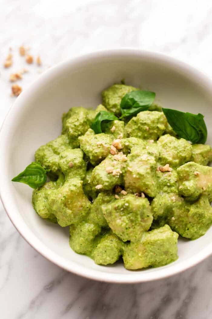 bowl of creamy pesto gnocchi with fresh basil and crushed walnuts on top.