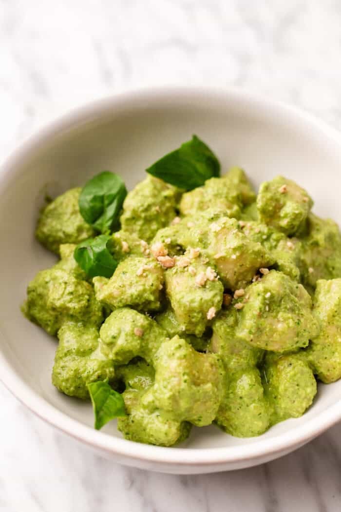 bowl of pesto gnocchi with walnuts on top.