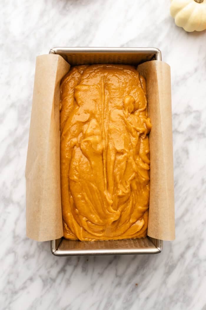 pumpkin bread before baking in a loaf tin on a marble table.
