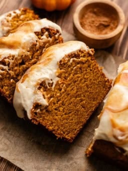 sliced vegan pumpkin bread slices leaning on each other with a small bowl of cinnamon sugar next to it on a wooden table.
