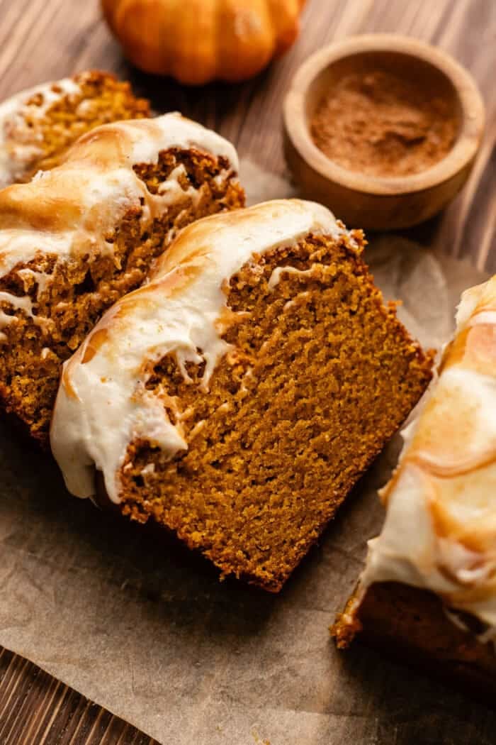sliced vegan pumpkin bread slices leaning on each other with a small bowl of cinnamon sugar next to it on a wooden table.