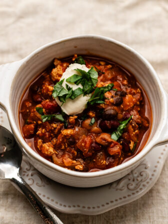 bowl of vegan pumpkin chili with sour cream on top on a plate with a cloth napkin underneath.