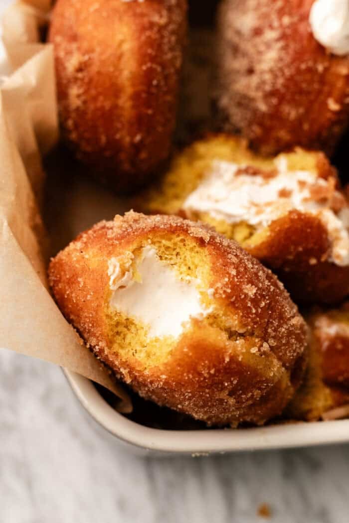 bitten pumpkin doughnut in a container with other doughnuts around it.